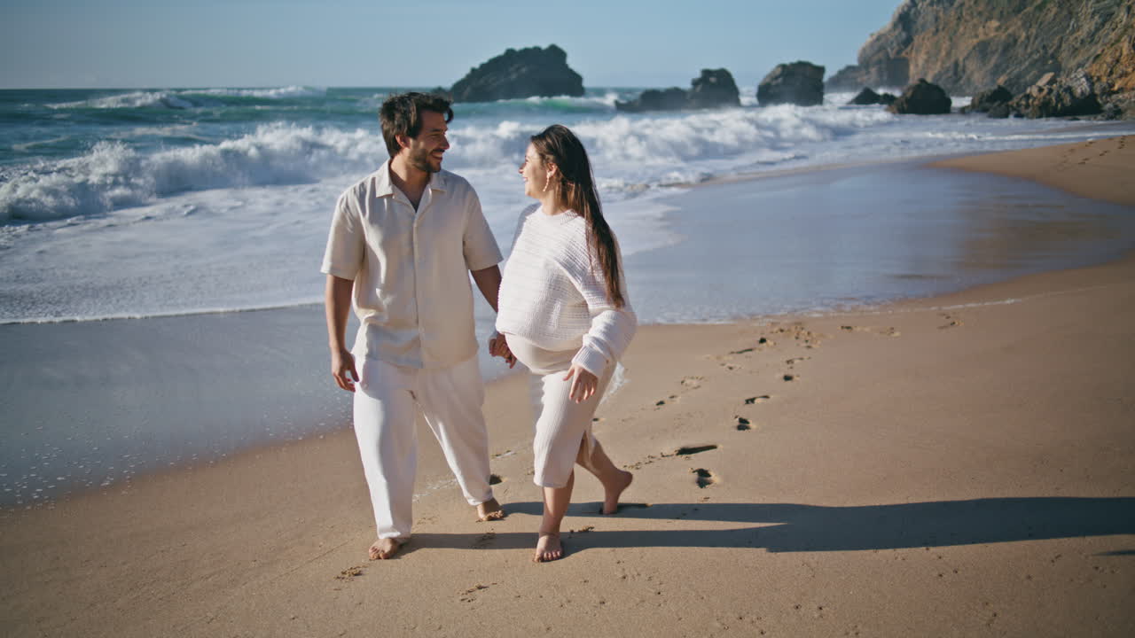 임신 한 가족 은 해변 에서 산책 하는 것 을 즐기며 미소 짓고 있다. 해변 에서 아기 를 기다리고 있는 부부