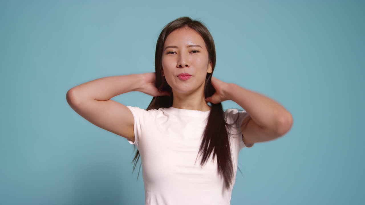 푸른 스튜디오 배경 앞의 젊은 여성이 사진 부스 스타일의 초상화를 위해 포즈를 취하고 있습니다.