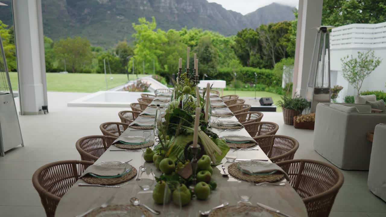 An elegant table setting on the undercover veranda of a luxury house with a beautiful garden and mountain as the backdrop
