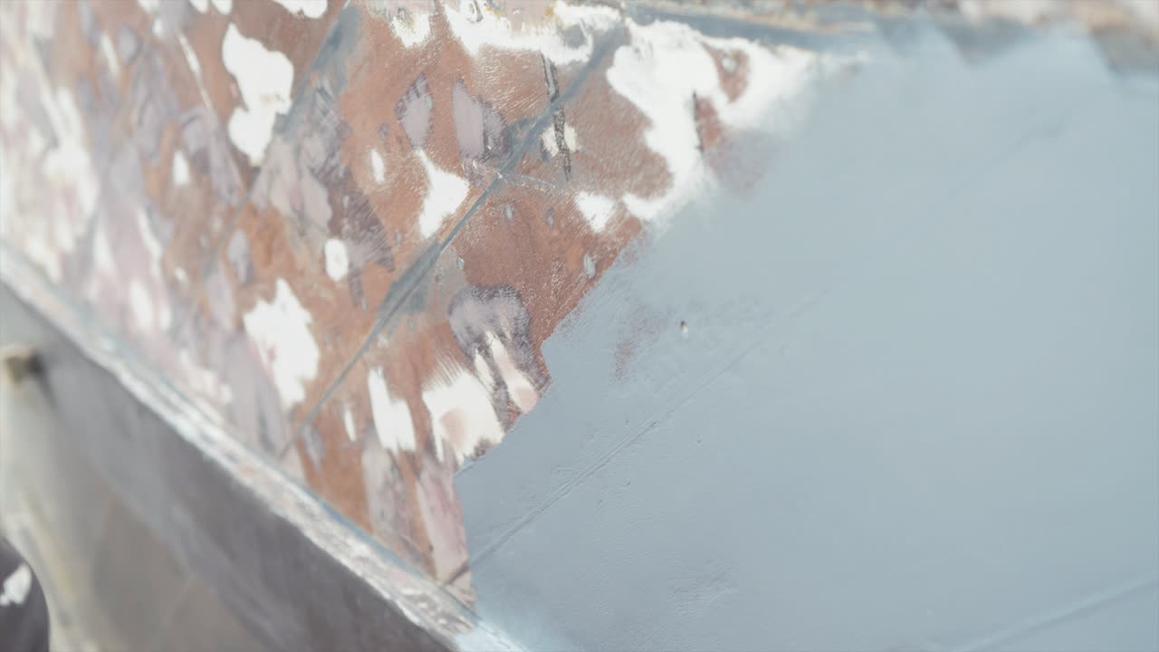 кавказский мужчина рисует корпус шлифованной старой лодки с роллом для краски, взгляд вблизи