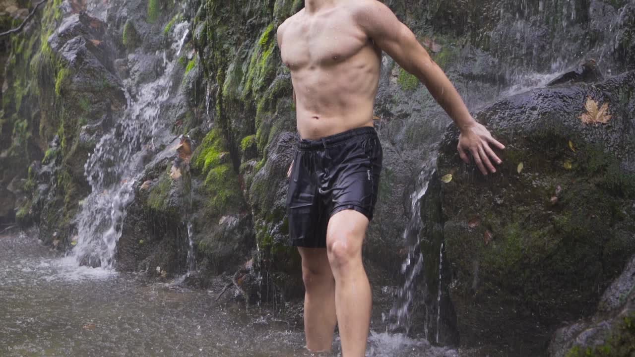 hombre musculoso mojándose debajo de una cascada.