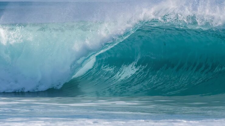 Swell pushing turquoise wave curling into barrel on nearshore reef, lifting spray and whitewater