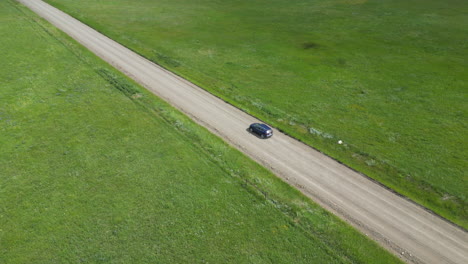 Ein-Blaues-Auto-Rast-Eine-Unbefestigte-Straße-Hinunter,-Auf-Deren-Beiden-Seiten-Grüne-Grasflächen-Liegen