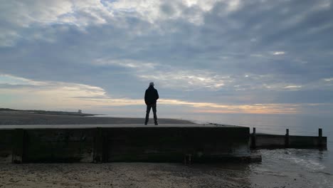 Low-angle-panning-shot-of-man-on-jetty-at-sunset-on-Fleetwood-Beach-Lancashire-UK