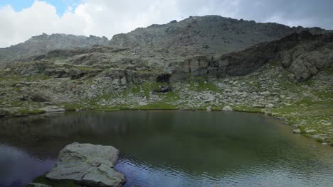 Idyllic-panning-shot-of-woman-pointing-to-a-peaceful,-small-pond-in-mountains-of-Valmalenco,-Italy