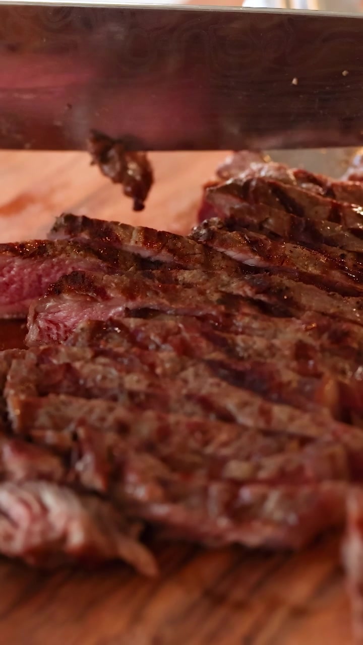 Primo piano di un coltello che taglia una bistecca alla griglia su un tagliere di legno, evidenziando la consistenza e la succosità sotto un'illuminazione calda.