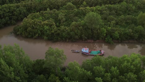 cinematic drone side shot of ship carrying small boat on amazon river surrounded by green rainforest trees during sunset