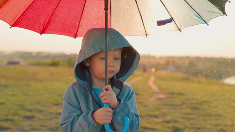 pensive kid with umbrella under rain at countryside offended little boy walks alone in green summer