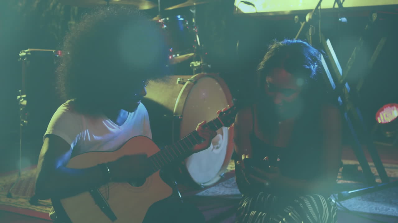 Man strumming guitar and woman checking smartphone on stage, with animated waveform and music chart