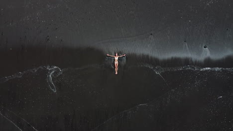 mujer relajándose en la playa de arena negra