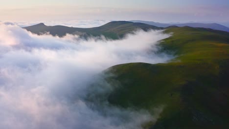 cloud-shrouded mountain hills at sunset, drone shot over foggy valley