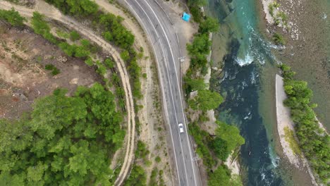 aerial view of a winding road next to a turquoise river through a forest