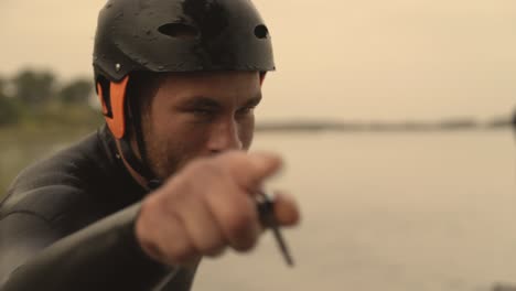 bearded male sports model in wetsuit with helmet looking straight into camera drops of water fall from face and point with finger in camera than turn away close up in slow motion