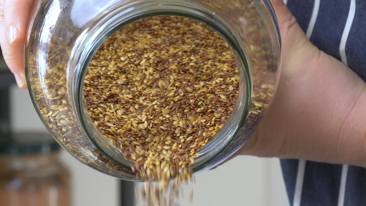 Brown and golden flaxseed pouring out of a glass jar in slow motion