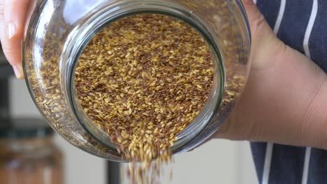 brown and golden flaxseed pouring out of a glass jar in slow motion