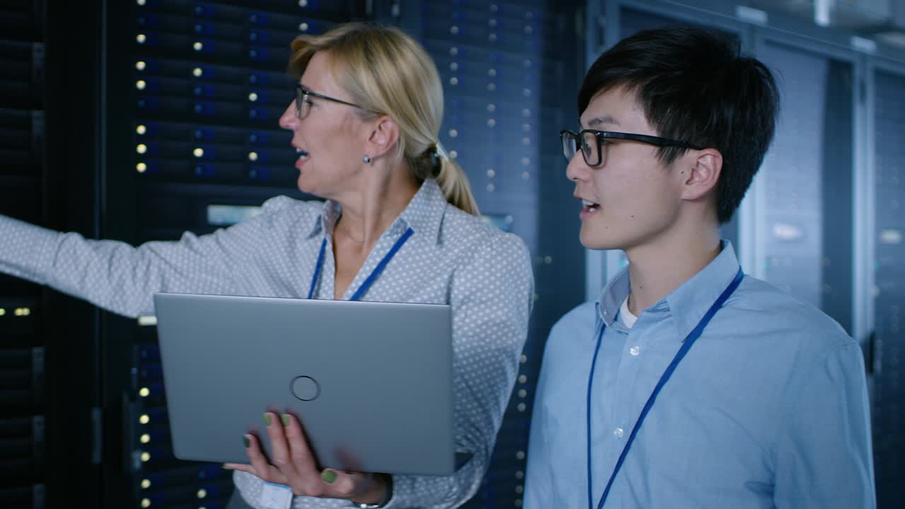 в современном центре обработки данных: инженер и ит-специалист работают с серверными стойками, разговаривают, проводят проверку обслуживания системы с помощью ноутбука. специалисты проводят диагностику базы данных.