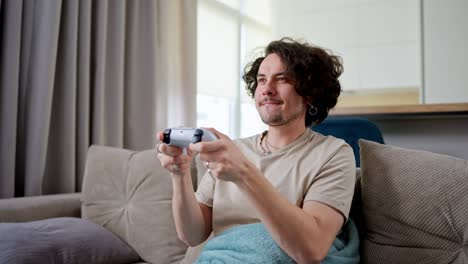 Happy-brunette-guy-with-curly-hair-and-mustache-plays-video-games-and-wins-with-a-joystick-and-sits-on-the-sofa-at-home-in-a-modern-apartment