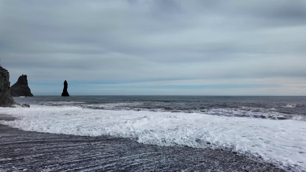 진정시키는 은 검은 모래 해변을 드러니다, 부드러운 파도가 어두운 구름 하늘 아래 평온의 느낌을 만니다.
