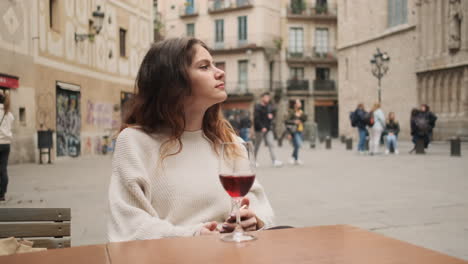 joven mirando a su alrededor mientras está sentada en un café con un vaso de vino rojo