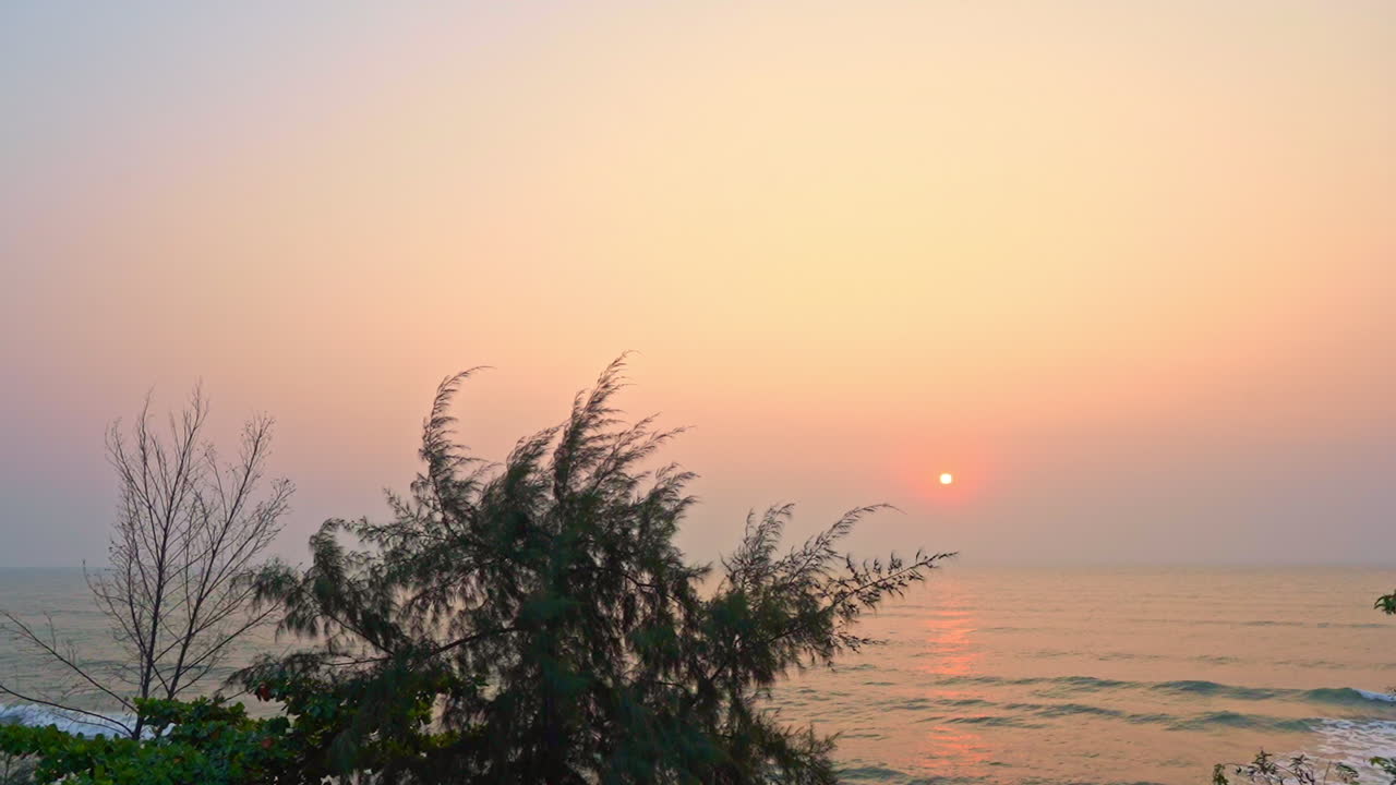 Stunning pink and purple pastel sunset sky on the horizon over a calm sea with small waves rolling toward shore of a tropical island paradise holiday destination. Slow motion