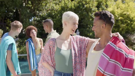 Portrait-of-happy-diverse-group-of-friends-embracing-and-holding-towels-in-summer