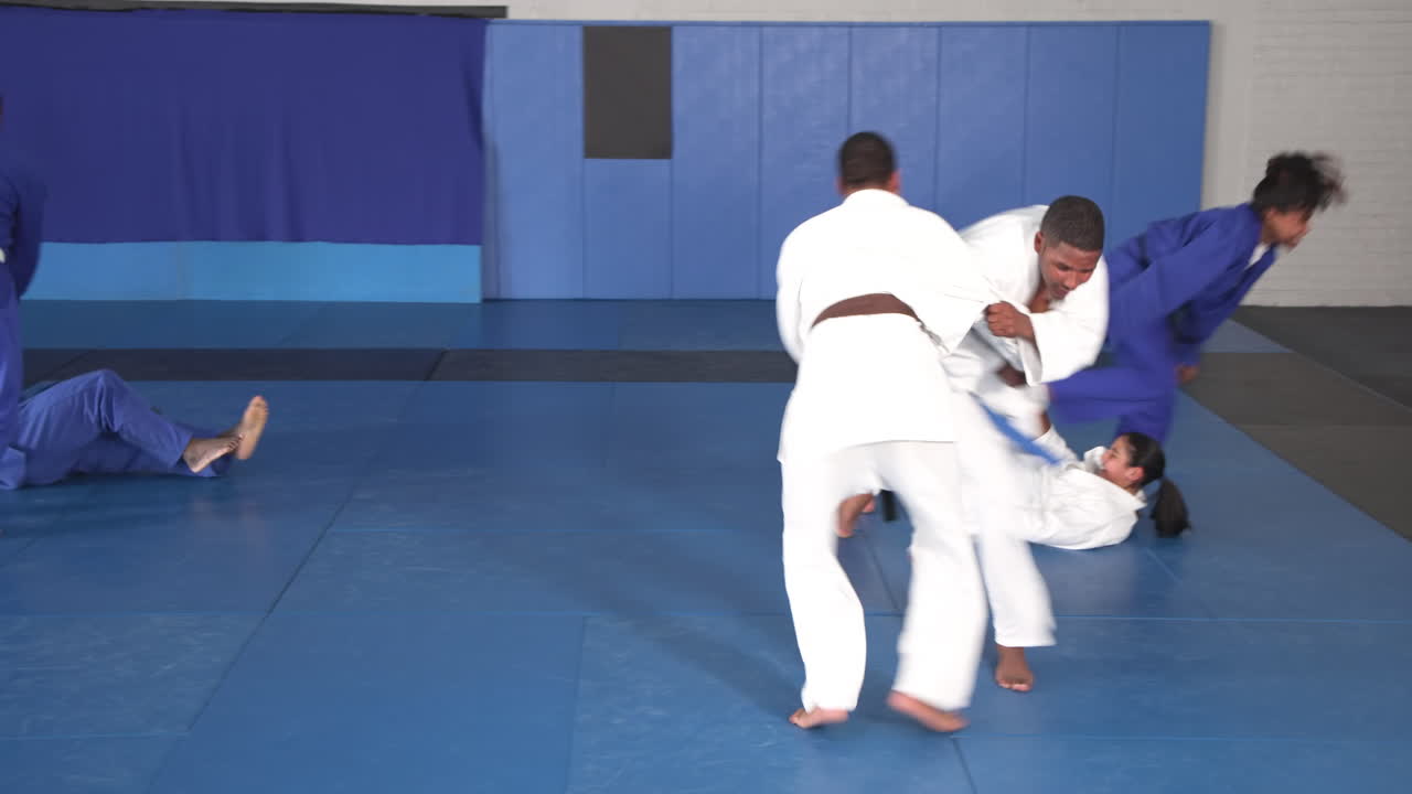 Practicing judo, athletes sparring on mats in martial arts school dojo