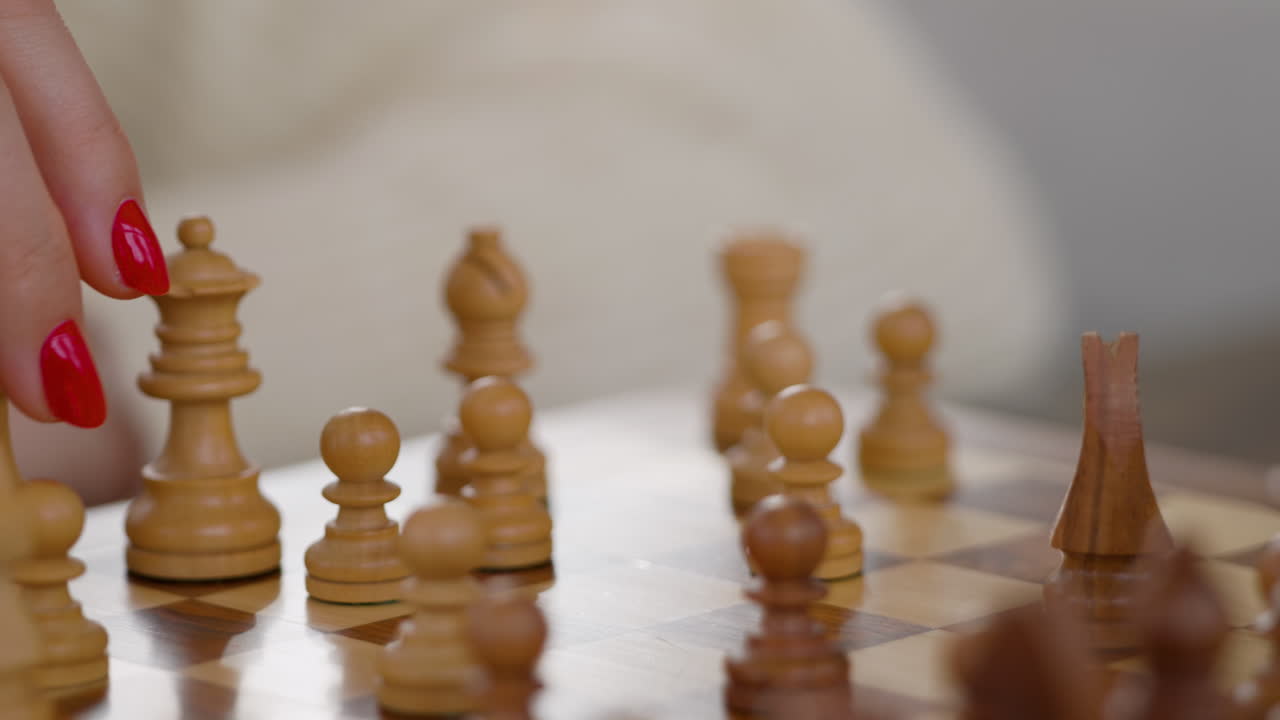 Una persona sposta un pezzo degli scacchi su una scacchiera di legno mentre gioca. L'ambientazione è un ampio salotto con altri pezzi degli scacchi in vista. L'attenzione è focalizzata sulla mano e sull'azione di gioco.