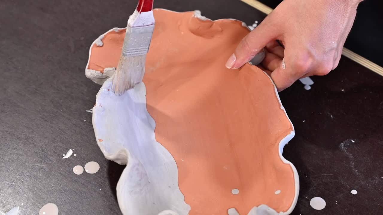 Woman painting an orange plate made out of clay with white