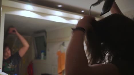 mujer morena caucásica se seca el pelo en el baño, su ídolo visible en el espejo
