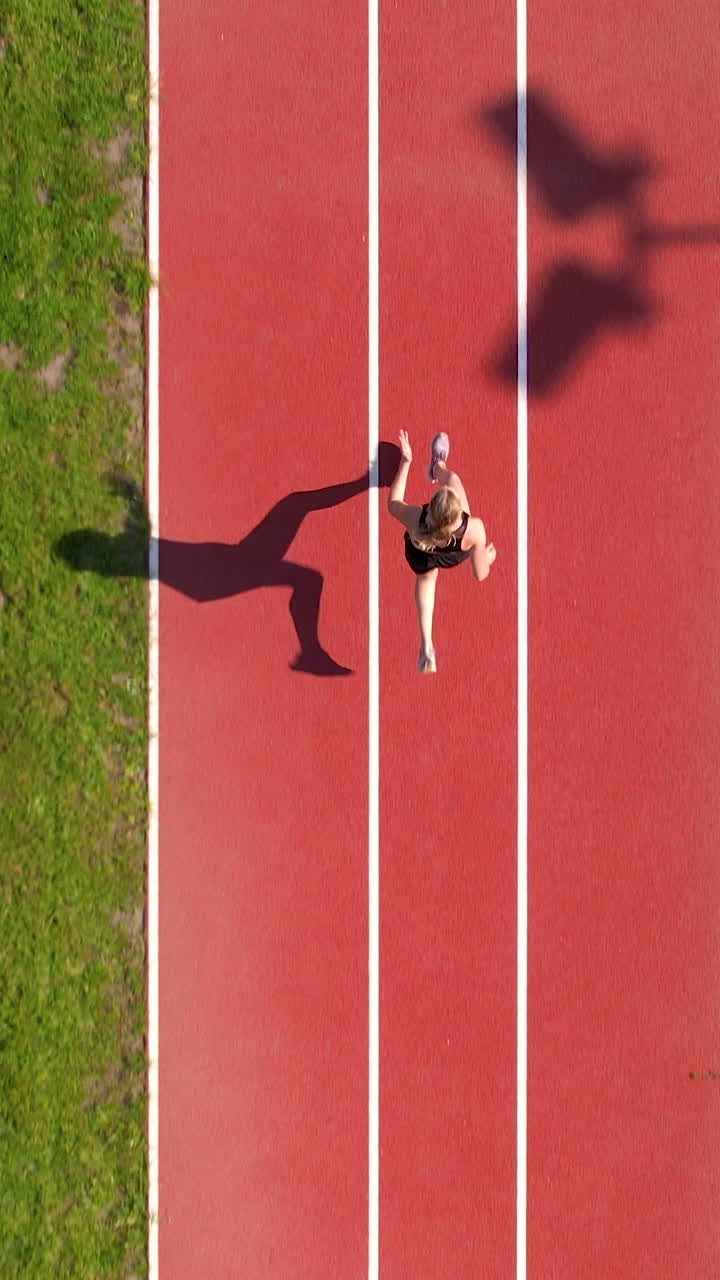 Ripresa aerea verticale di un'atleta che scatta su una pista da corsa in una giornata di sole. Perfetta per contenuti su fitness, sport e uno stile di vita sano.