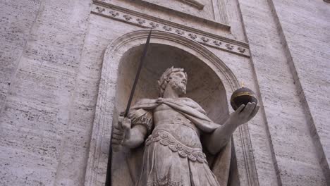 estatua de un emperador sosteniendo una espada y una reliquia, grabada en el muro de piedra blanca de una iglesia romana.