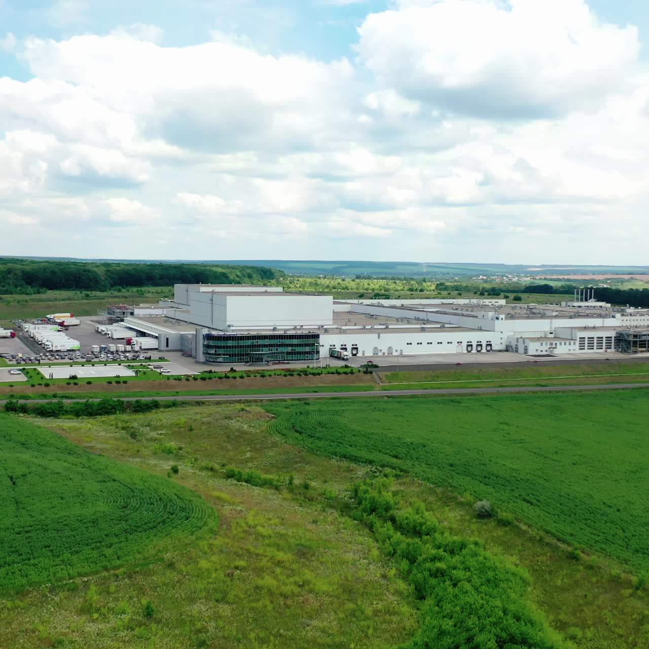 Modern factory on fields background. Huge industrial territory among green nature under beautiful sky. Front view of a manufacturing