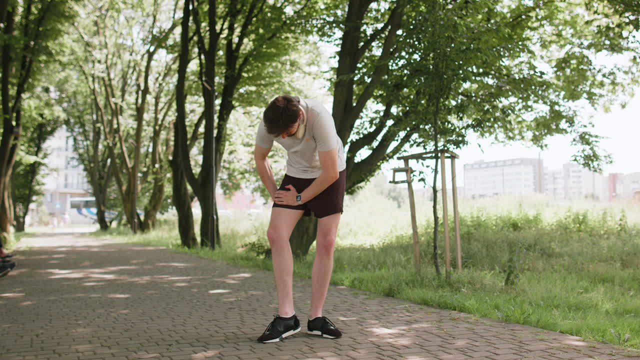 Young runner man athlete with muscle pain massaging stretching trauma injury while jogging in park