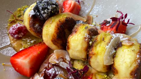 delicioso syrniki con bayas del bosque, virutas de plátano y coco en crema de anacardo y miel, sabrosos mini panqueques de queso para el desayuno, plato tradicional ruso ucraniano, tiro de 4k de cerca