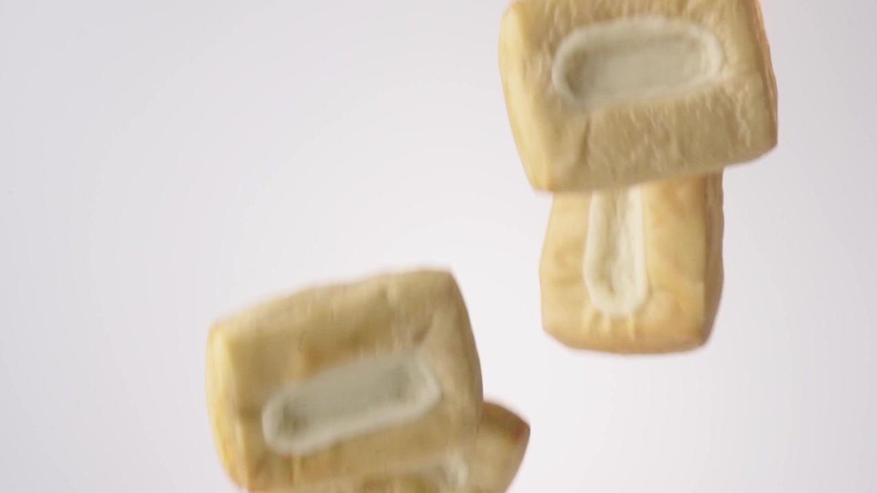 Shower of golden flaky cream-filled danishes falling on bright white studio backdrop in slow motion. danish brand commercials, pastry recipe content, weekend treat videos.