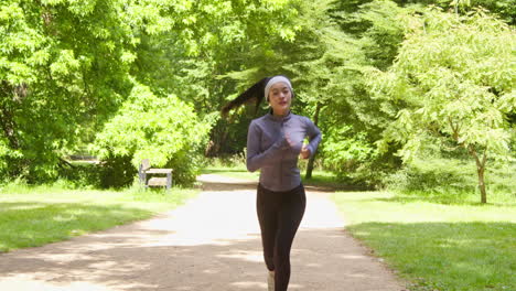 vista frontal de una mujer joven haciendo ejercicio corriendo por el parque de la ciudad usando auriculares inalámbricos