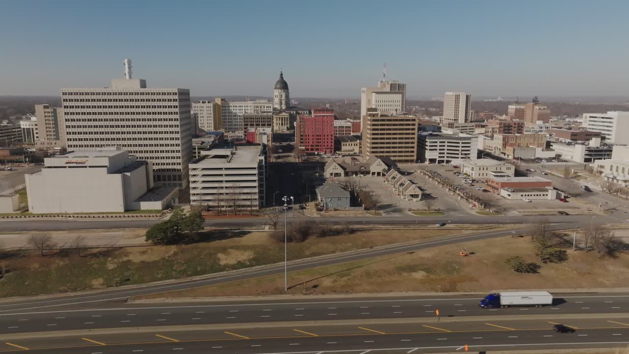 Luftaufnahme mit einer Drohne, die sich von rechts nach links bewegt und das Kansas State Capitol mit dem Autobahnverkehr in Topeka zeigt. Kinoreifes, etablierendes Filmmaterial, das Regierung, Transport und städtische Infrastruktur hervorhebt