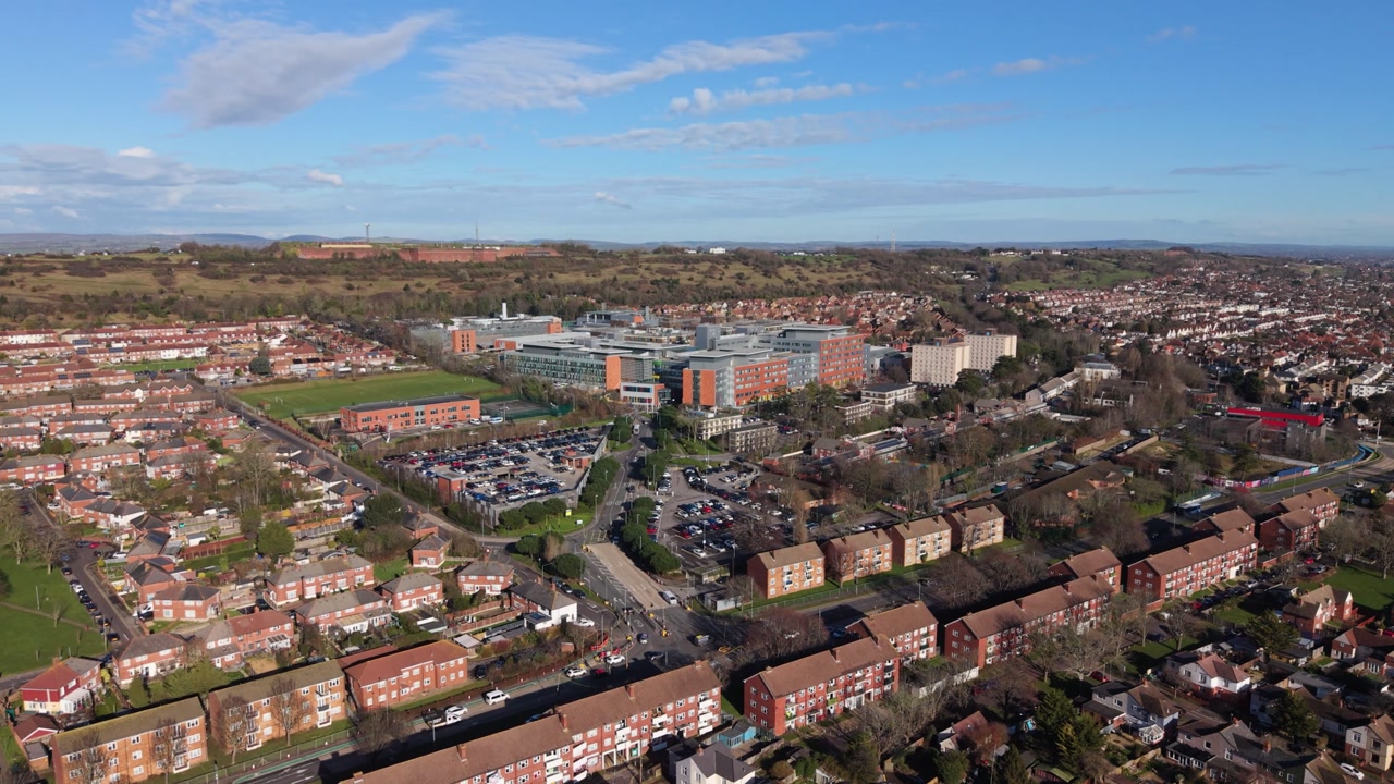 Portsmouth slow dropping drone flight directly towards Queen Alexandra Hospital at the base of Swanick Hill with distant countryside views in bright sun flying over housing estates and green spaces