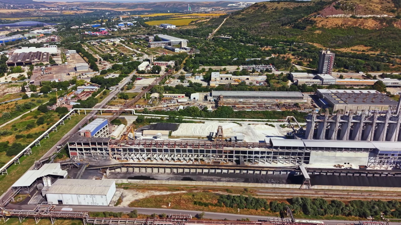 Gran complejo industrial con silos y maquinaria ubicado en una zona rural durante el día, con edificios y carreteras visibles en el paisaje circundante.