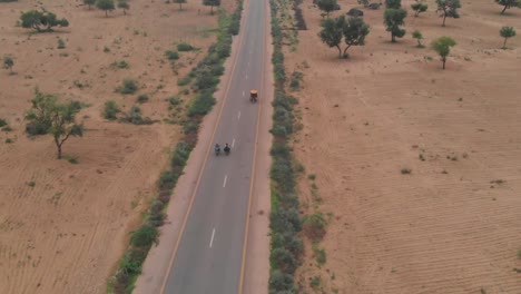drone takes an aerial shot of the two biker driving their bike in the highway of tharparkar near sindh and passing by a rickshaw