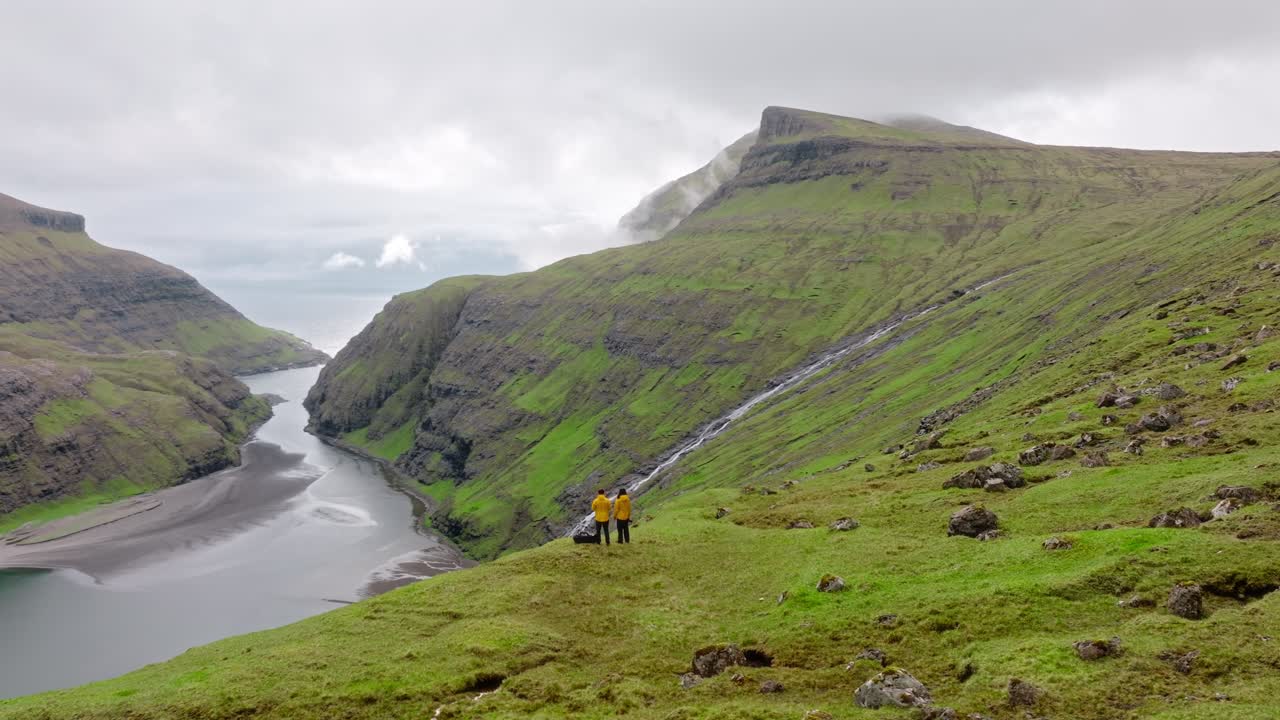 A serene view of the Faroe Islands, with green valleys, cliffs, and hikers outdoors