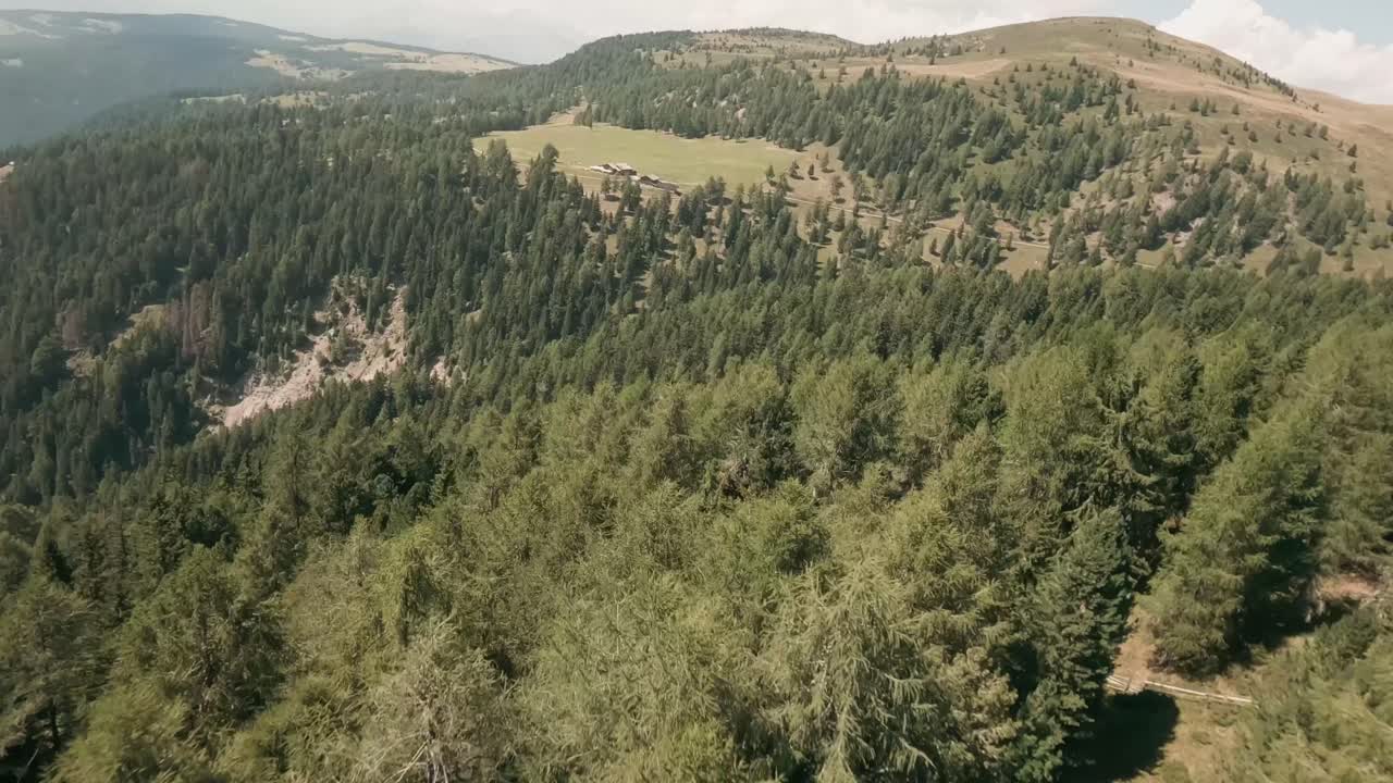 un dron fpv captura impresionantes vistas aéreas sobre las cimas de los árboles del bosque de abetos, revelando una rústica cabaña de madera en medio del paisaje escénico cerca de la aldea de luzen, italia