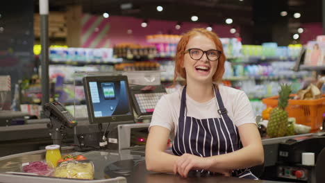 young sales clerk woman laughing behind cash box in a supermarket