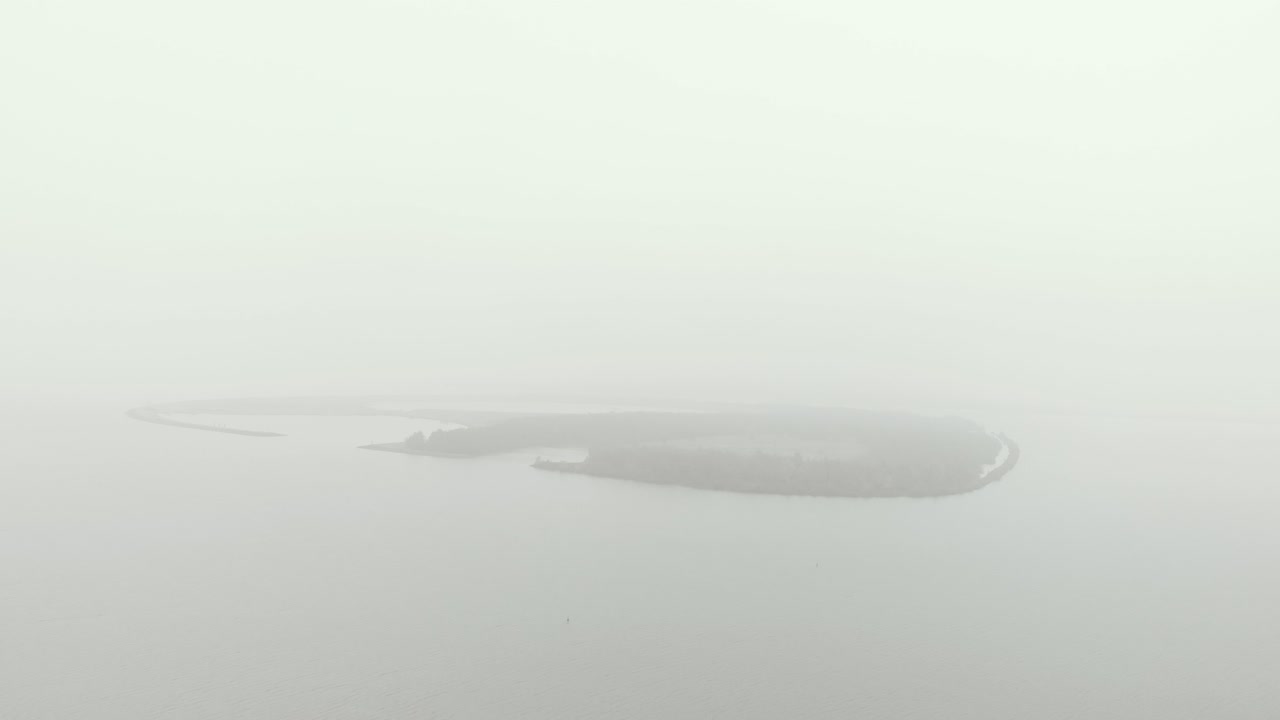 lento acercamiento aéreo de una isla misteriosa y cubierta de bancos de niebla de forma ovalada en un clima de día monótono totalmente nublado y gris