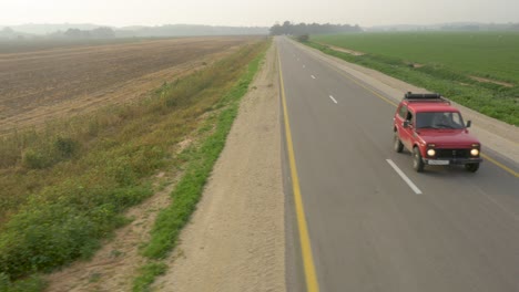 aerial tracking red suv car driving on road beside farm fields
