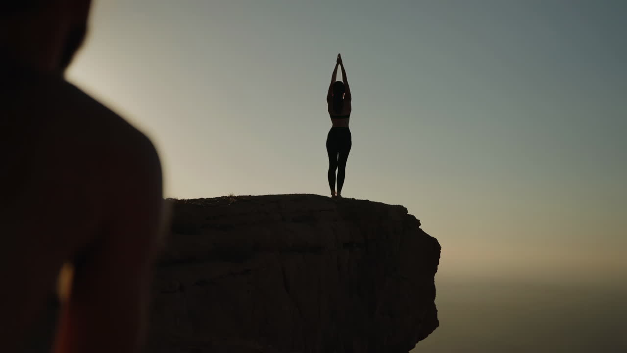 Person practicing yoga on a cliff edge at sunrise or sunset