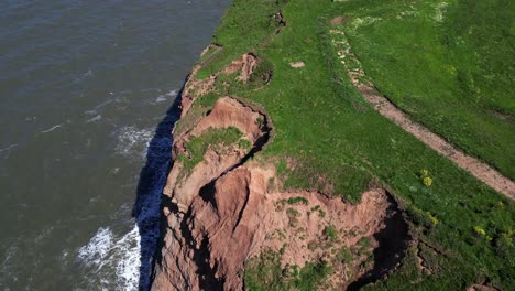 rising drone reveal of large ocean waves crashing on rocky cliffside on sunny summers day in north yorkshire coast at staithes