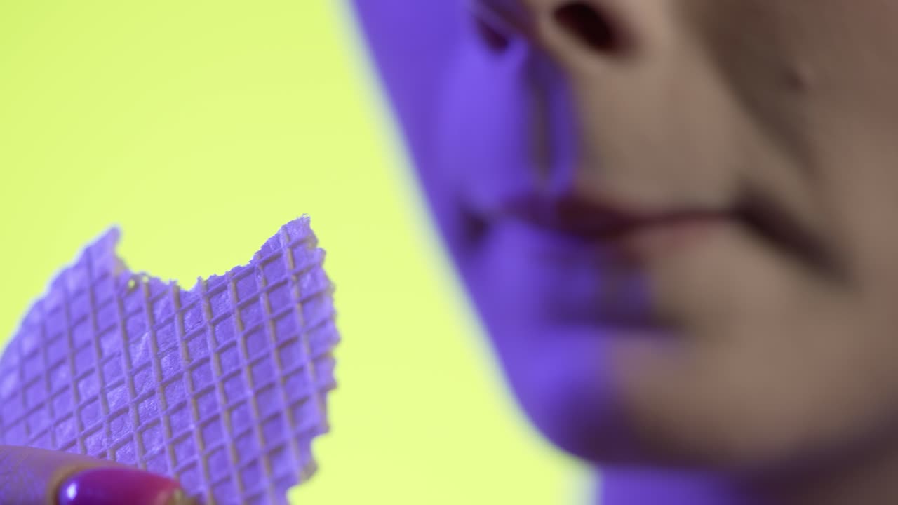 mujer comiendo un waffle crujiente en primer plano, esmalte de uñas femenino y labios de lápiz labial rojo sobre fondo verde