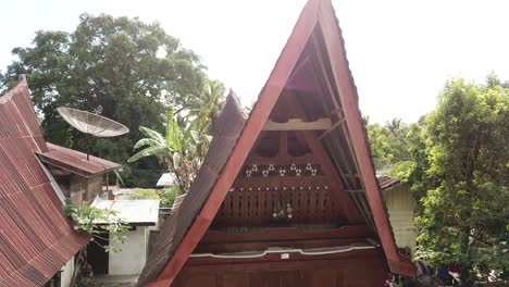 Drone-rising-in-front-of-a-traditional-Batak-house-on-Samosir-Island-in-lake-Toba,-Sumatra,-Indonesia