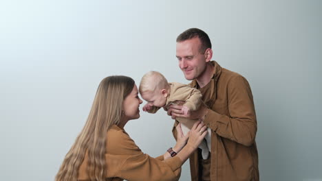 cheerful caucasian parents playing with their little baby. happy family of three spending time together. white backdrop.